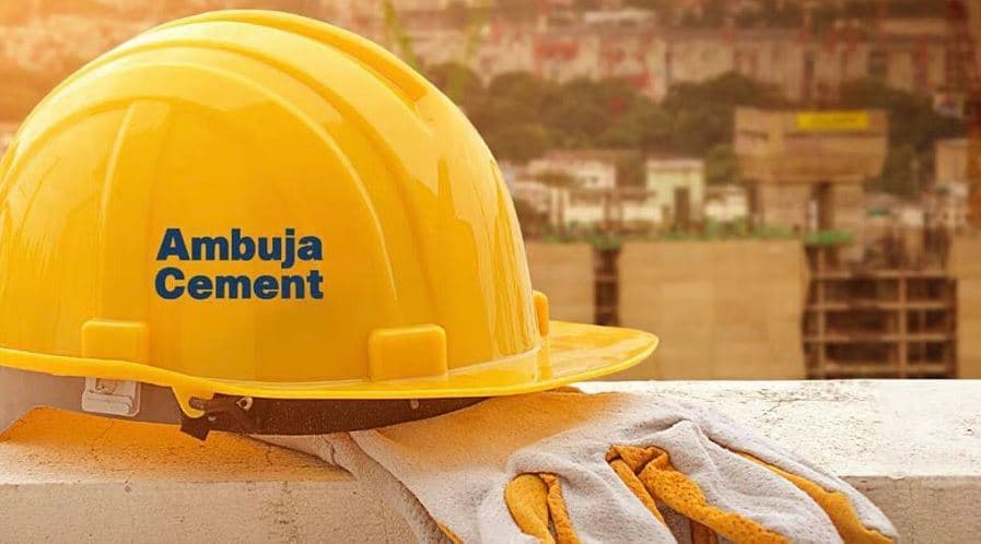 Yellow Ambuja Cement hard hat resting on a construction site ledge with gloves beside it.