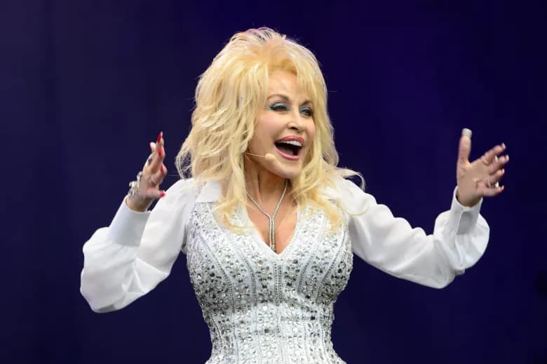 Dolly Parton singing on stage in white rhinestone outfit with arms raised