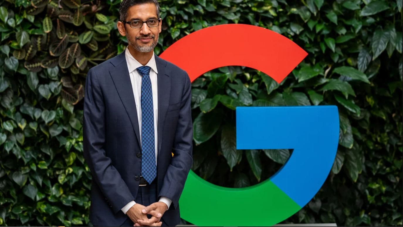 Sundar Pichai standing in front of Google logo representing leadership in global technology and AI innovation