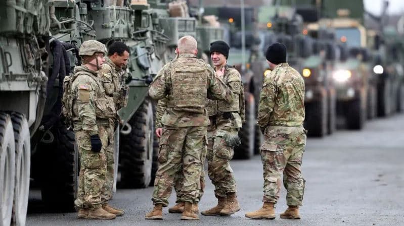 U.S. soldiers stand beside military vehicles during a deployment operation in Europe, amid rising NATO tensions and discussions over potential troop reductions in Germany.